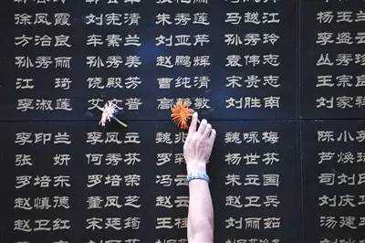 7月28日，一名唐山市民将鲜花粘附在遇难亲人的名字旁。新华社记者 牟宇 摄